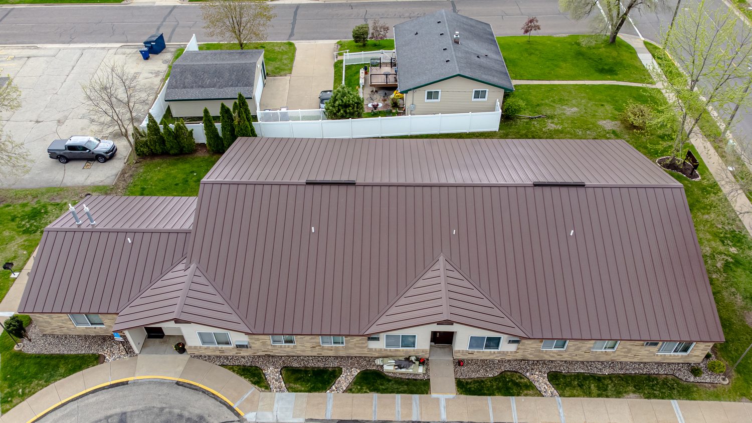 Aerial view of a standing seam metal roof with hips, valleys and an asphalt-roofed house visible nearby